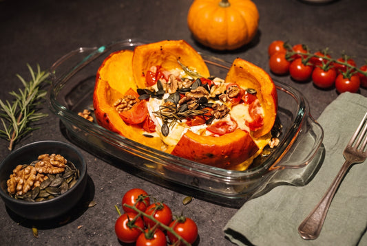 Stuffed Hokkaido pumpkin, cut open in a glass baking dish, with melted brie, cherry tomatoes, rosemary, activated walnuts and pumpkin seeds